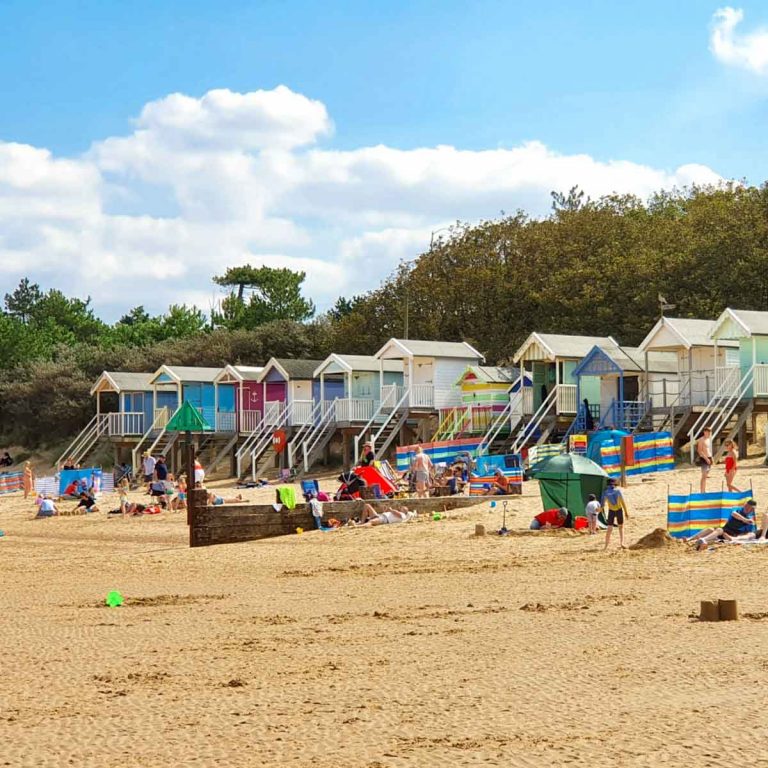 Sunbathers and beach huts on the beach at Wells-next-the-Sea - visiting is one of the top things to do in Norfolk with kids
