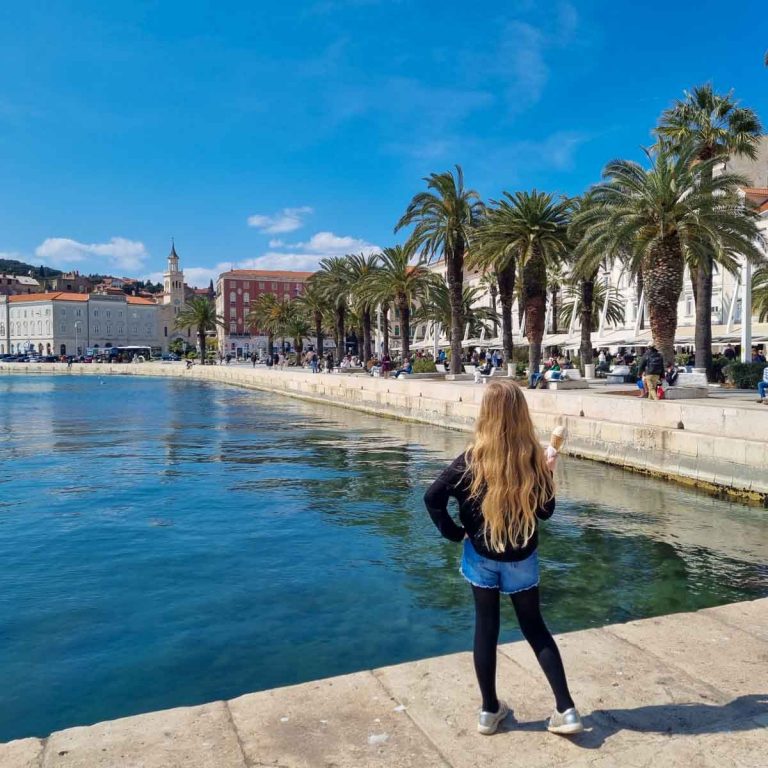 My daughter holding an ice cream looking along the Riva waterfront promenade lined with palm trees to some of the old buildings of Split - my pick of the best things to do in Split with kids