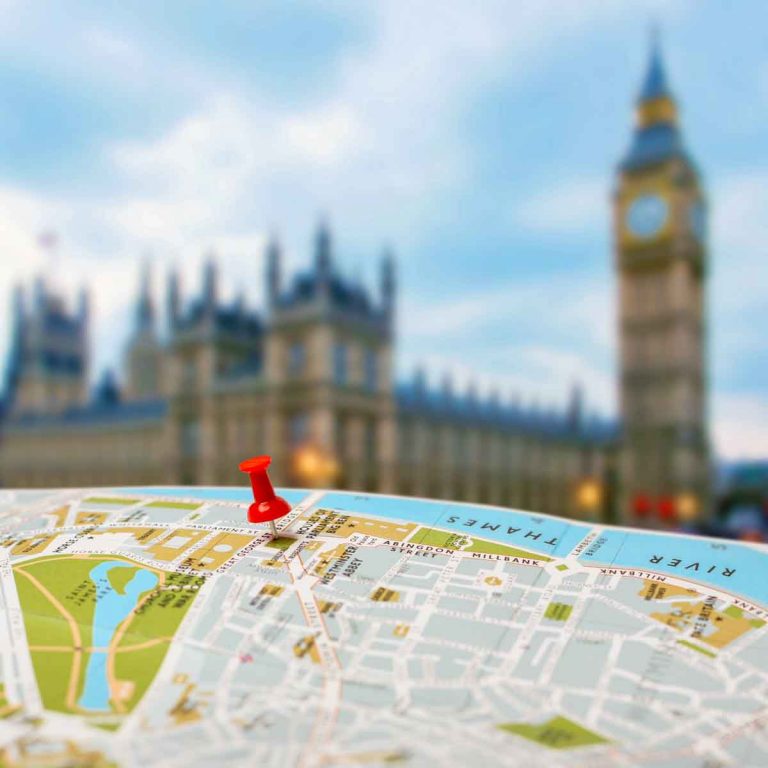 Red push pin in a London city map with the Houses of Parliament and Big Ben blurred in the background - my self-guided London landmarks walking route taking you on a London sightseeing walk past the city's iconic sites.