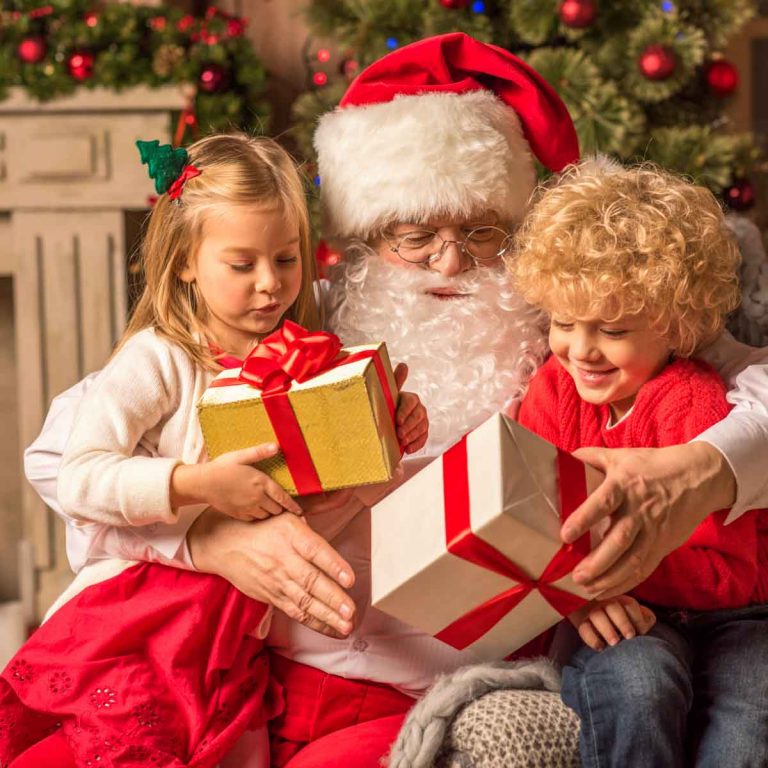 Girl and a boy sit on Santa's knee holding presents with decorations in the background - my top picks for where to see Santa in London with kids