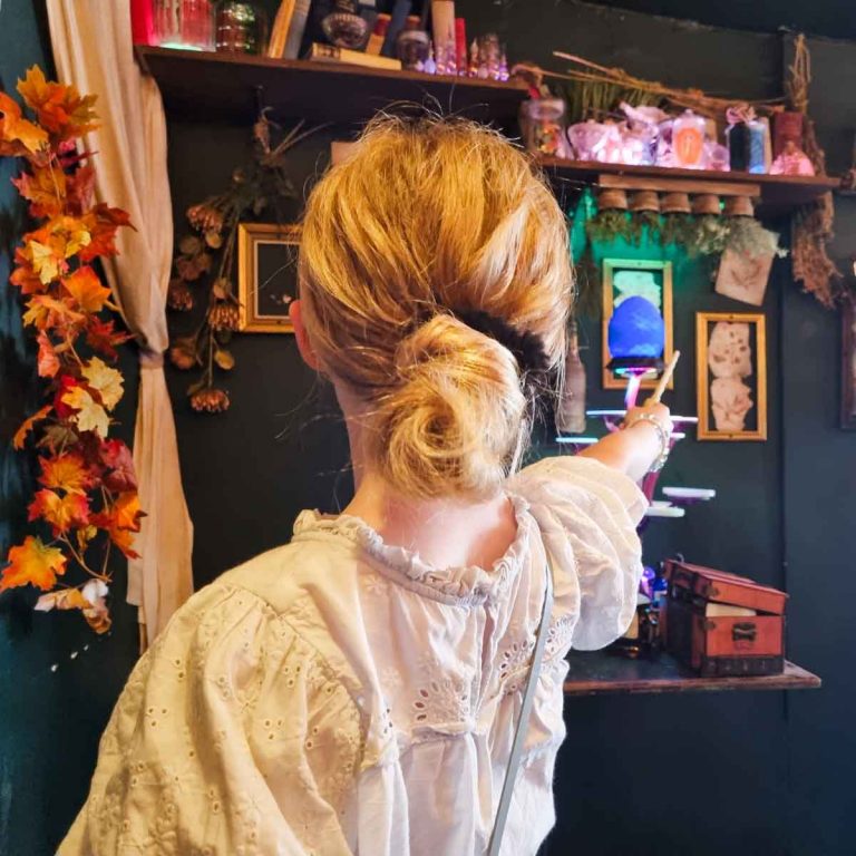My daughter points a wand towards an illuminated blue dragon's egg and upside down plants, among other decorations seen on the walls and shelves of the Wizard Exploratorium before our Wizard Afternoon Tea London with kids