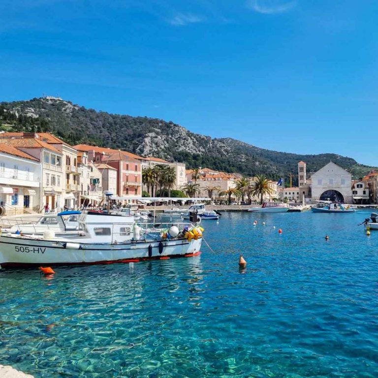 View of boats in the harbour of Hvar Town with the pastel coloured buildings and hills in the background - how to spend one day on Hvar with kids on a day trip from Split