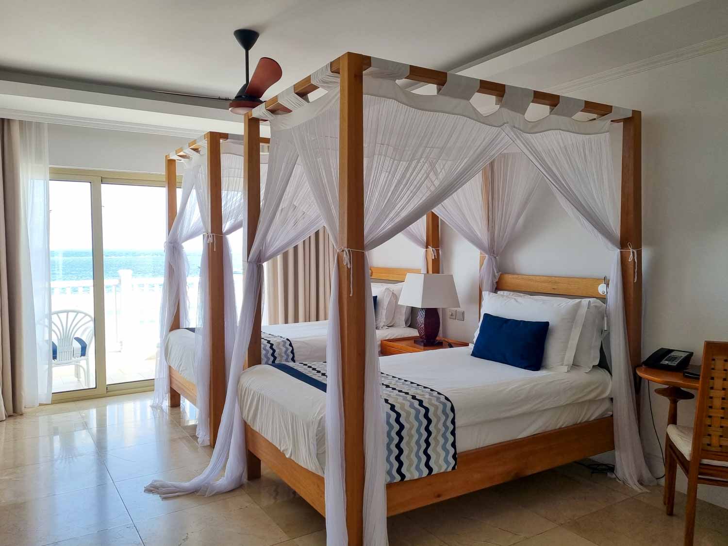 View of our four-poster double beds with mosquito nets and blue cushion detail in our Deluxe Ocean View room at Hemingways Watamu - my review of Hemingways Watamu with kids