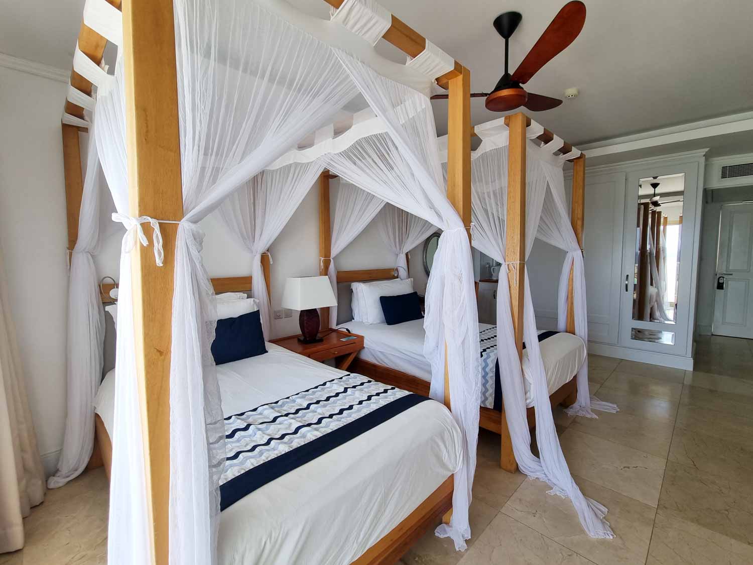 View of our four-poster double beds with mosquito nets and blue cushion detail in our Deluxe Ocean View room at Hemingways Watamu - my review of Hemingways Watamu with kids