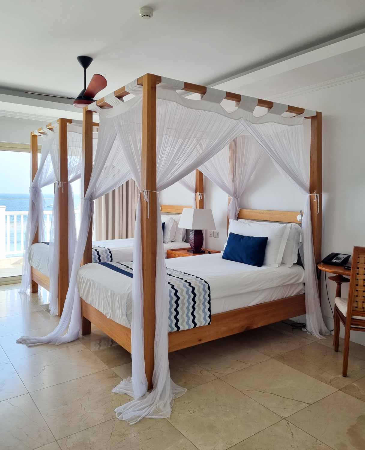 View of our four-poster double beds with mosquito nets and blue cushion detail in our Deluxe Ocean View room at Hemingways Watamu - my review of Hemingways Watamu with kids