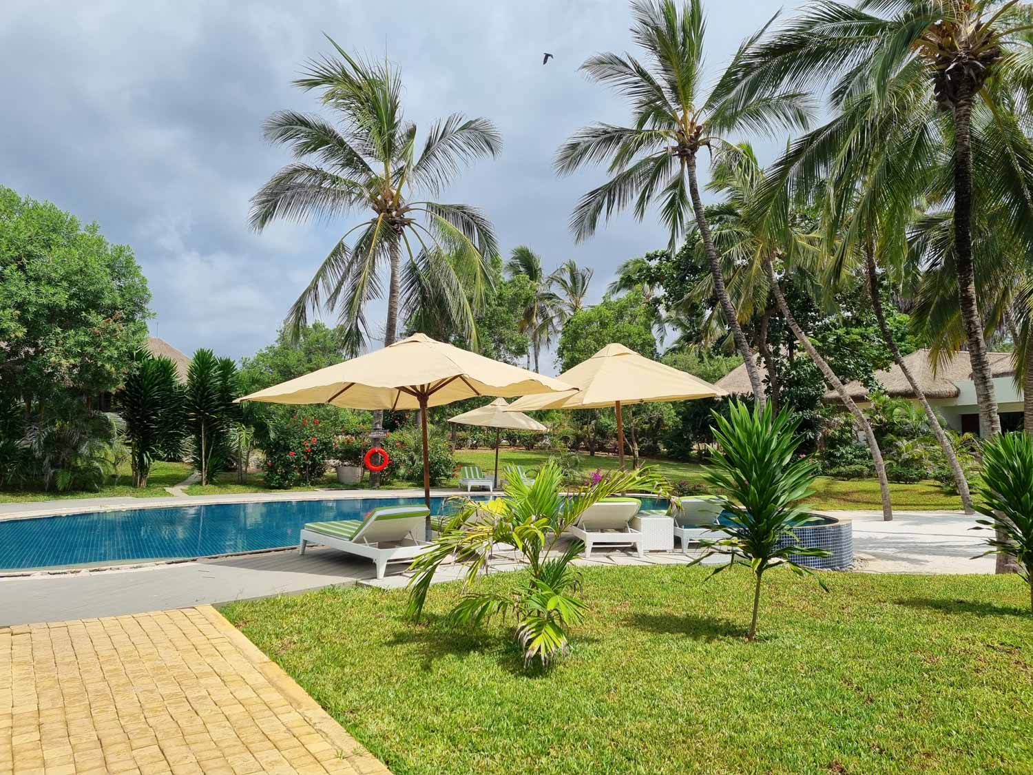 View towards the quiet pool with its loungers and umbrellas, overshadowed by palm trees - our favourite spot during a stay at Hemingways Watamu with kids