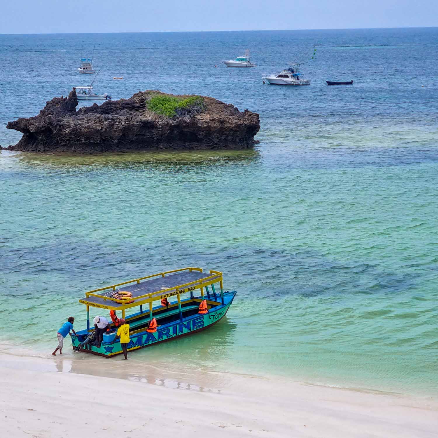 Small colourful boat on the beach by Hemingways Watamu, being pushed into the turquoise waters of the Indian Ocean - one of many boats taking tourists out to spot dolphins and snorkel the reefs