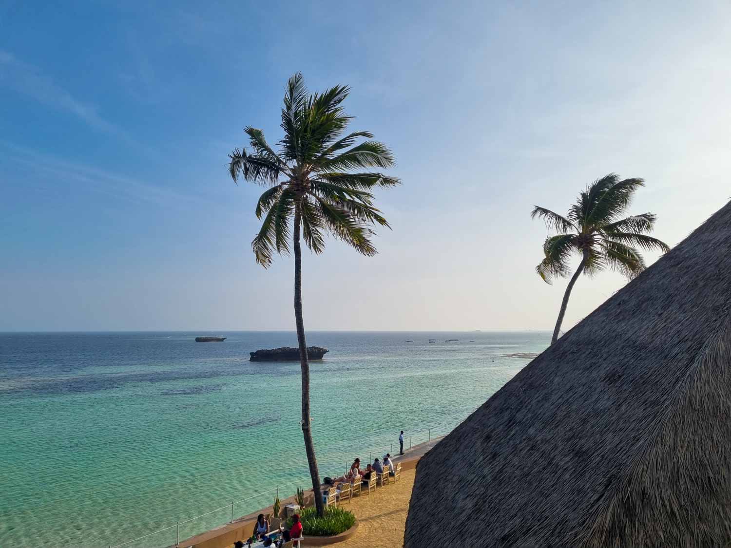 View from our balcony to the paved walkway overlooking the sea, with palm trees seen against a blue sky - my Hemingways Watamu review