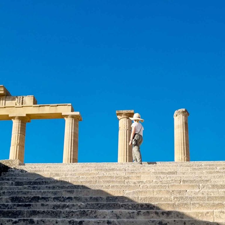 My daughter walks up the step at Lindos Acropolis to some of the columns remaining from the ancient temples - a visit is one of the best things to do in Rhodes with kids