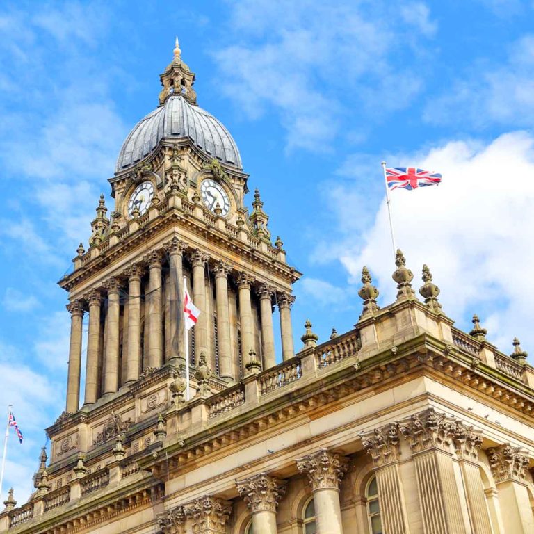 View of Leeds town hall with flags flying against a blue sky - a great place for a family city break, I've picked my top things to do in Leeds with kids