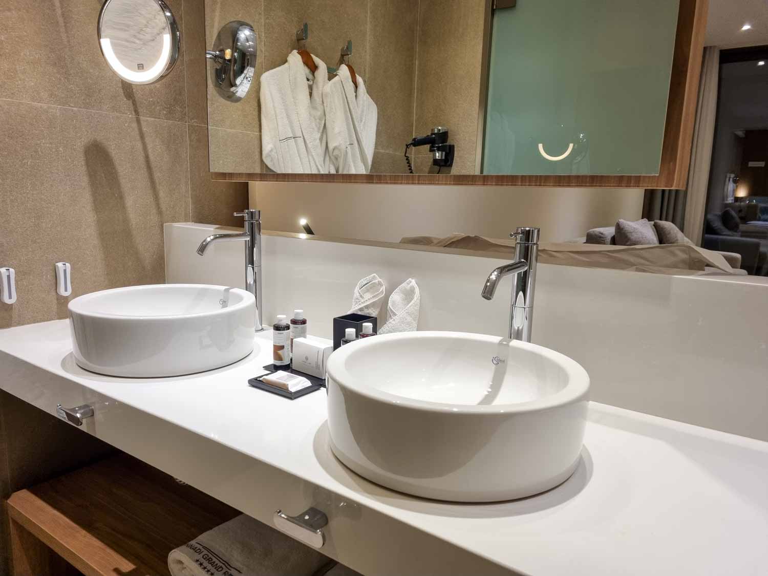 View of the bathroom in our Junior suite at Gennadi Grand resort, looking across the sinks and mirror, through a small open area towards the bed and living area - my Gennadi Grand review