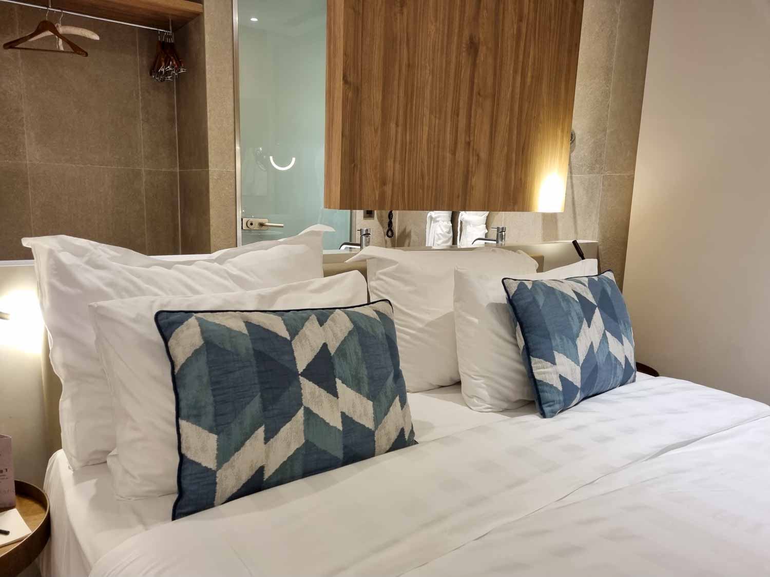 Pillows and blue patterned cushions on the double bed of our Junior Suite at Gennadi Grand resort in Rhodes with the bathroom and hanging area behind - my Gennadi Grand review of a Rhodes hotel for families