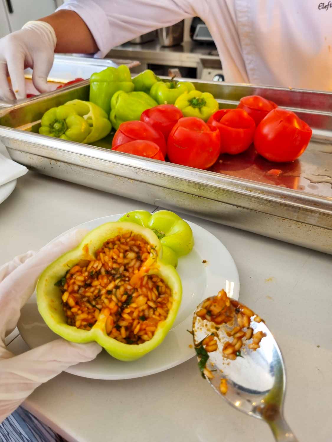 My daughter holds a green pepper stuffed with rice as part of a cooking lesson at Gennadi Grand resort, a silver tray of green peppers and tomatoes in the background - my Gennadi Grand Resort review of a family-friendly hotel in Rhodes