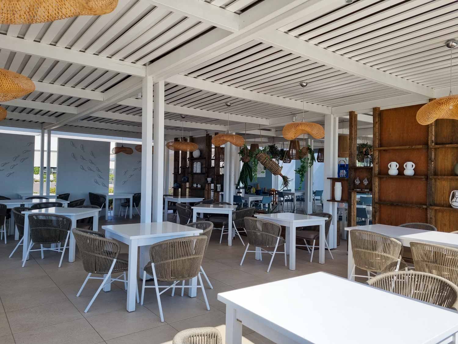 View of Ouzo restaurant by the pool at Gennadi Grand Resort with wicker-style seats around white tables - my Gennadi Grand Resort review