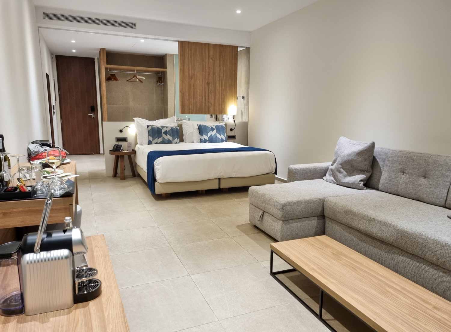 View of the bed and living area of a Junior suite at Gennadi Grand Resort in Rhodes, with double bed and double sofa bed, bathoom just seen - my Gennadi Grand review