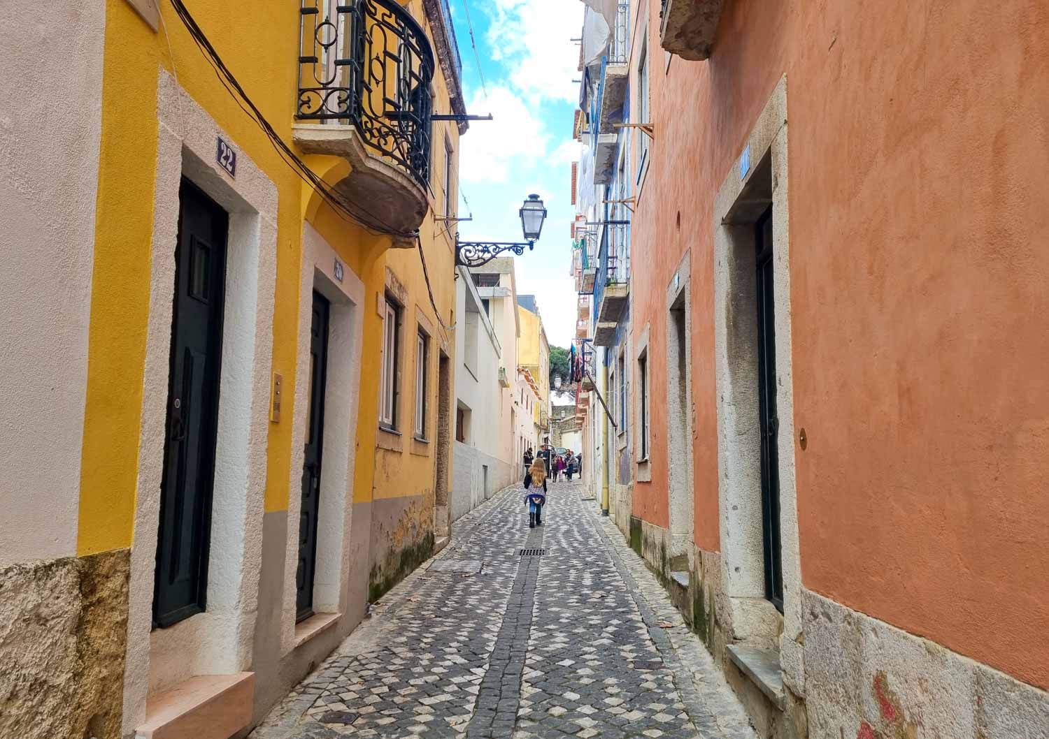 My daughter walks past colourful houses up one of the cobbled hilly streets in Lisbon's Alfama district - taking a walking tour is a great start to a visit to Lisbon with kids