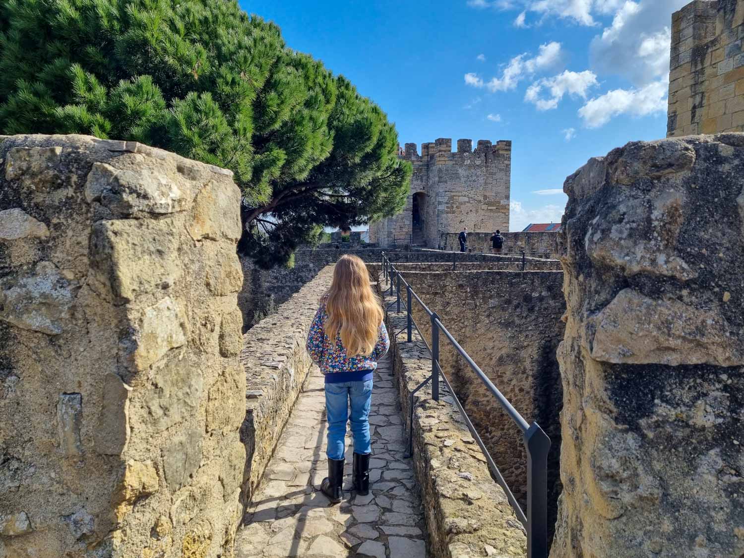 My daughter walks along the walls of Castelo de Sao Jorge, the historic castle in Lisbon on a sunny day - one of my top things to do in Lisbon with kids