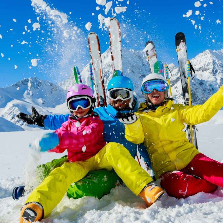 Family of three sitting in the snow with skis and blue sky behind - the best family ski resorts in France