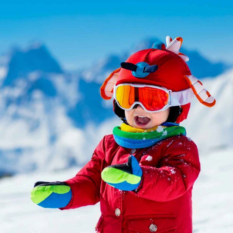 Grinning young child in winter clothes in the snowy mountains - my tips for choosing a family ski holiday with childcare