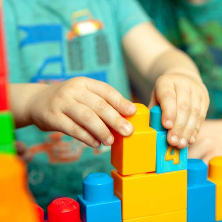 Child`s hands piling blocks up with toys spread around - my top toddler travel toys that should go into your hand luggage