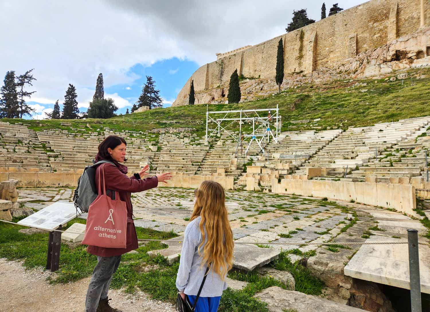 My daughter listens to our Alternative Athens tour guide at the temple of Dionysus at the start of our Acropolis tour with kids