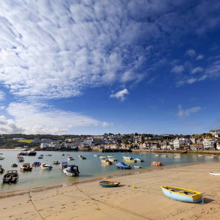 View of fishing boats on the beach and the buildings of St Ives in Cornwall beyond the sea - my top things to do in St Ives with kids