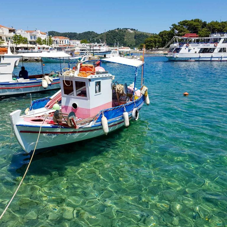Pink, white and blue boat on the clear green water of the harbour at Skiathos Town in Greece - my pick of the best things to do in Skiathos with kids