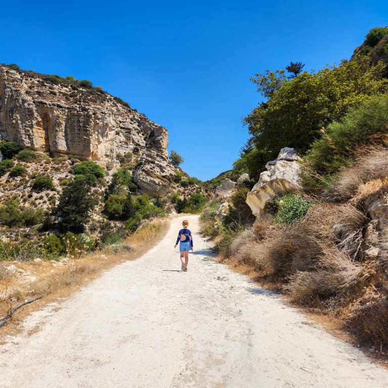 My daughter walks along a dusty rough track between the rocky hills during our tour of Akamas National Park and Avakas Gorge with kids in Cyprus