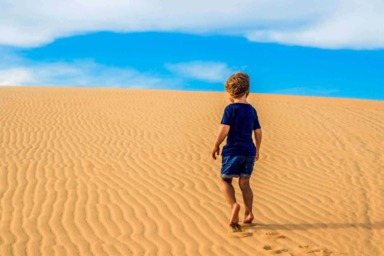 Boy climbs up a sand dune towards the blue sky - week in Oman itinerary with kids
