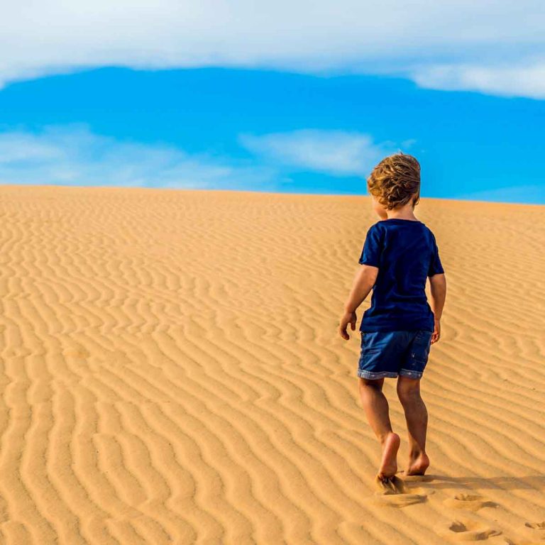 Boy climbs up a sand dune towards the blue sky - week in Oman itinerary with kids