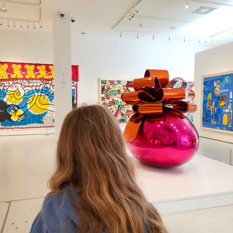My daughter looks at the colourful artworks in the ground floor gallery, including pieces by Jeff Koons and Keith Haring - my review of Moco Museum London with kids
