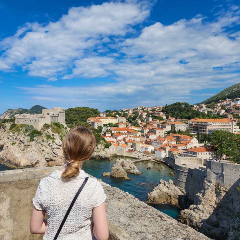 My daughter looks down onto the clear water of the west harbour with Fort Bokar and Lovrijenac both visible - my guide to the Dubrovnik walls with kids