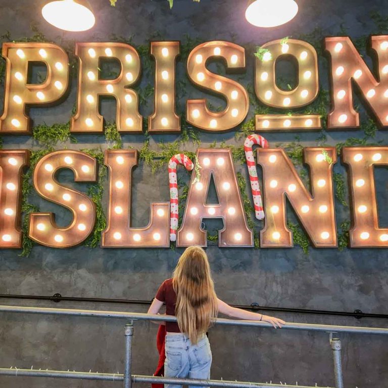 My daughter stands under the illuminated Prison Island sign - my review of Escape from Prison Island with kids