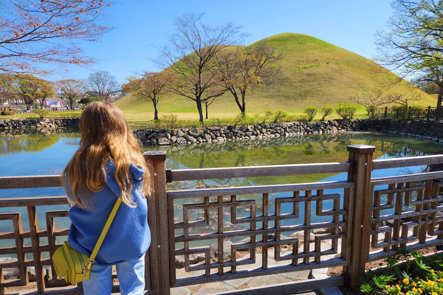 My daughter looks out across the water to a double mounded hill containing royal tombs from the Silla empire in Gyeongju - the best things to do in Gyeongju with kids