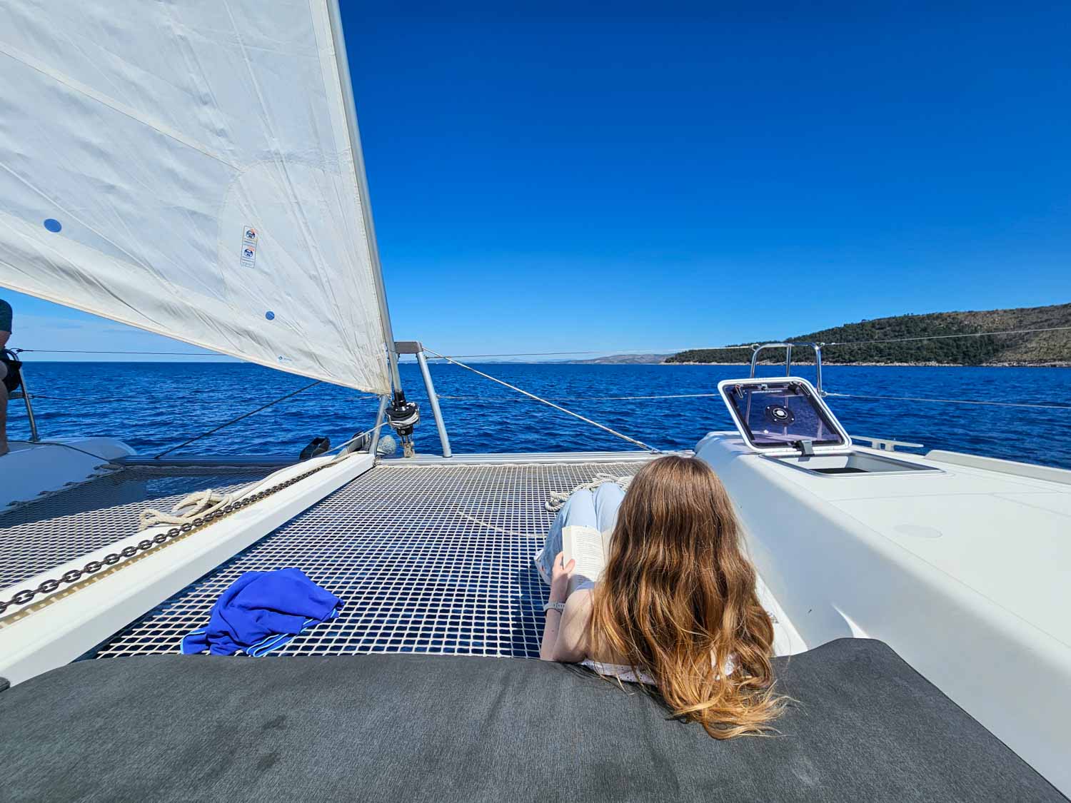 My daughter relaxes with a book on the nets at the front of our Lagoon 42 catamaran on a More Sailing Croatia holiday - my review of a Croatia sailing holiday with kids