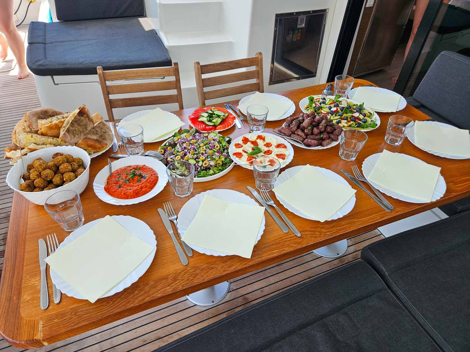 View of lunch aboard our More Sailing catamaran, including salads, Croatian bread, vegetarian options and meat during a Croatia sailing holiday with kids