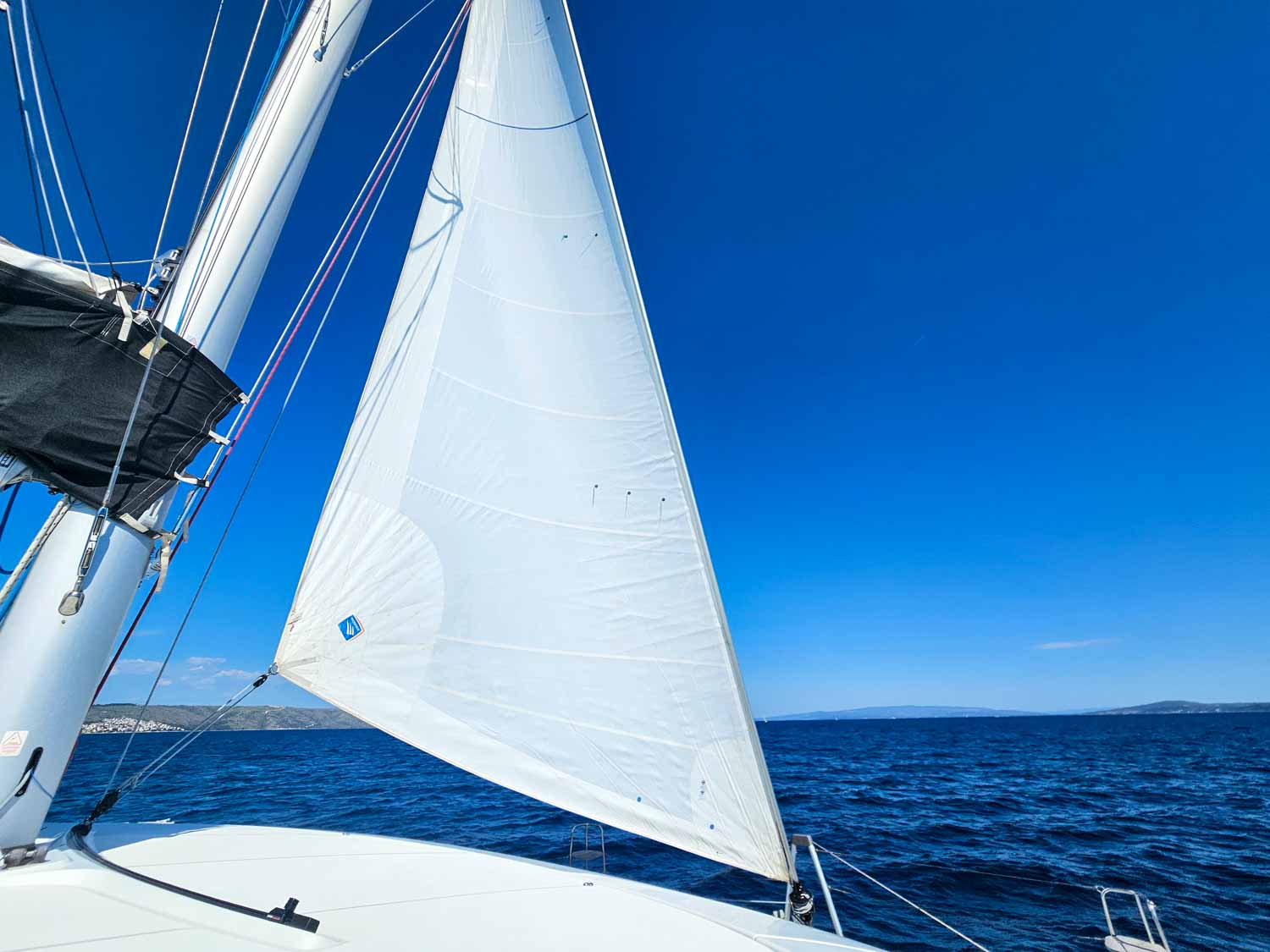 View of the smaller sail and front of the catamaran to dark blue water and blue skies during our Croatia sailing holiday with kids