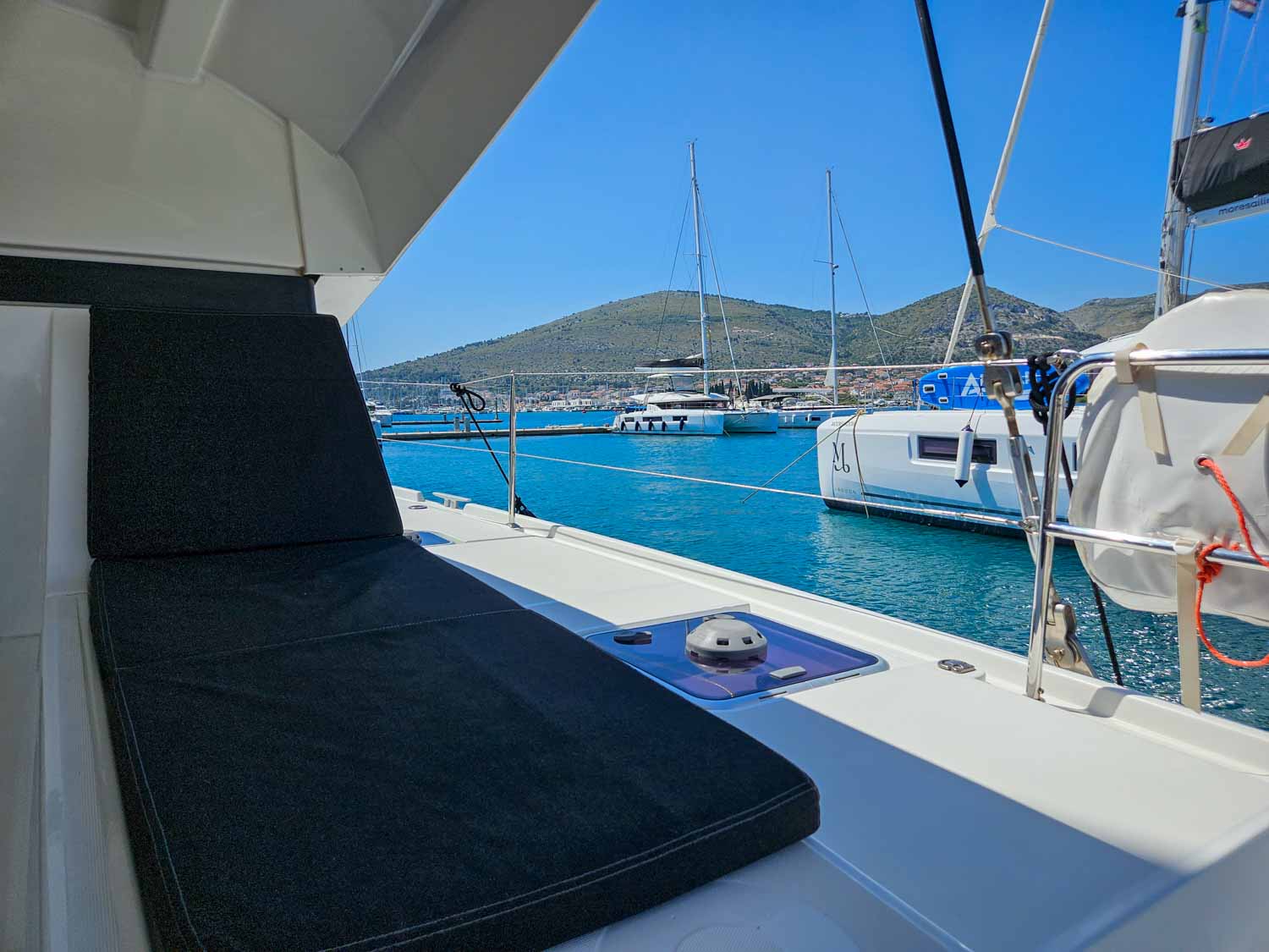 View of one of the shaded cushioned seats at the back of the catamaran, with other boats moored at Trogir marina just seen - my More Sailing Croatia review