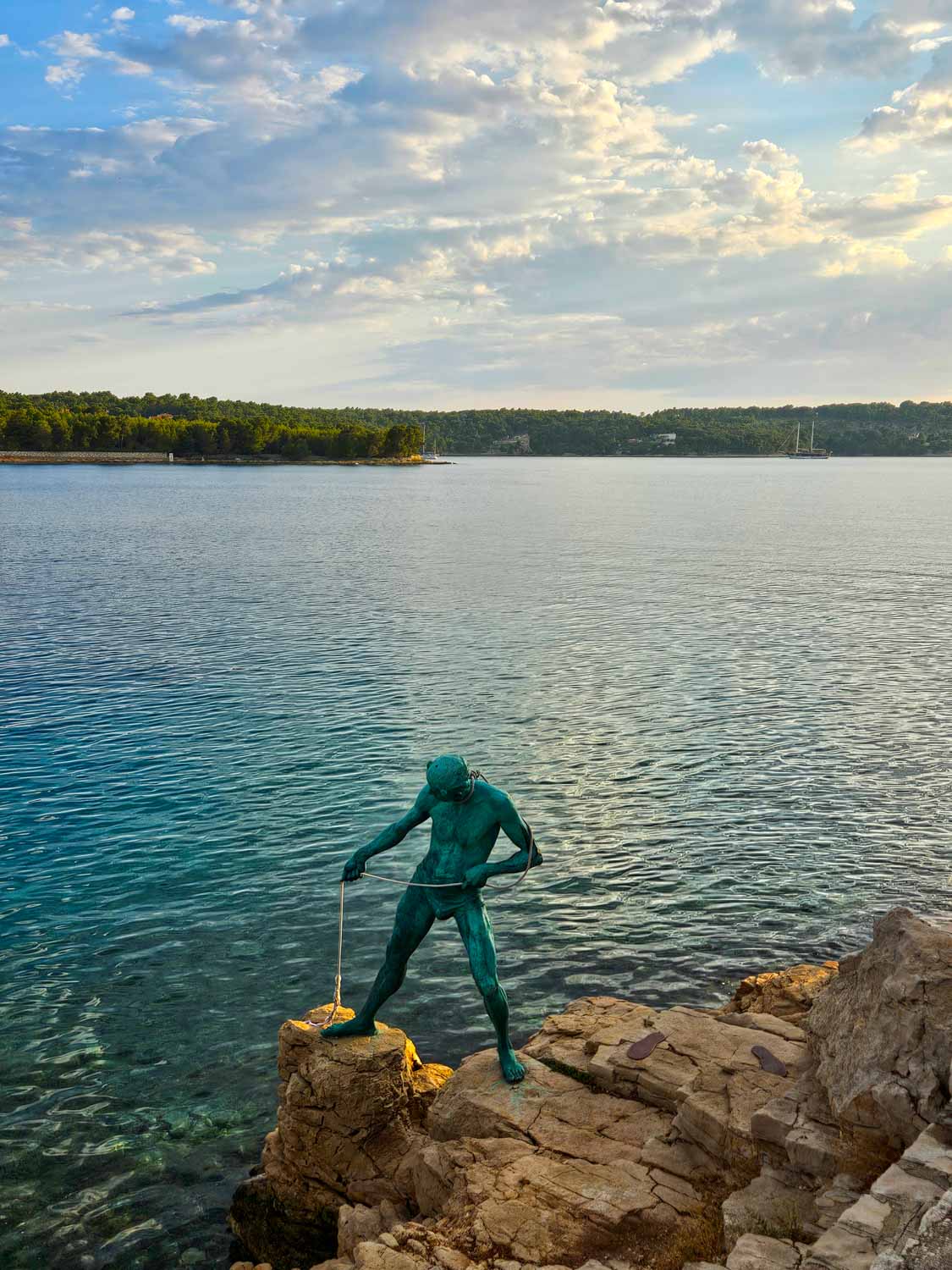 A statue green with verdigris of a man pulling a rope from the water on a rocky promontory at Milna on Brac, the first stop on our Croatia sailing holiday with kids