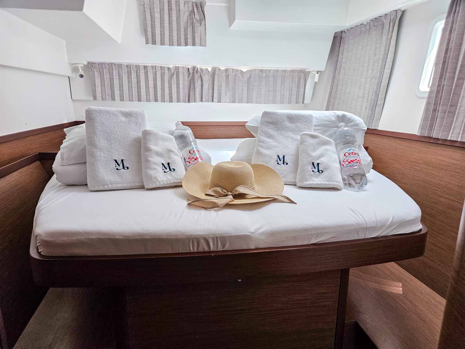 View of our double bed with towels, water, pillows and a sun-hat, curtains closed in the cabin aboard our Lagoon 42 catamaran - my review of a More Sailing Croatia holiday with kids