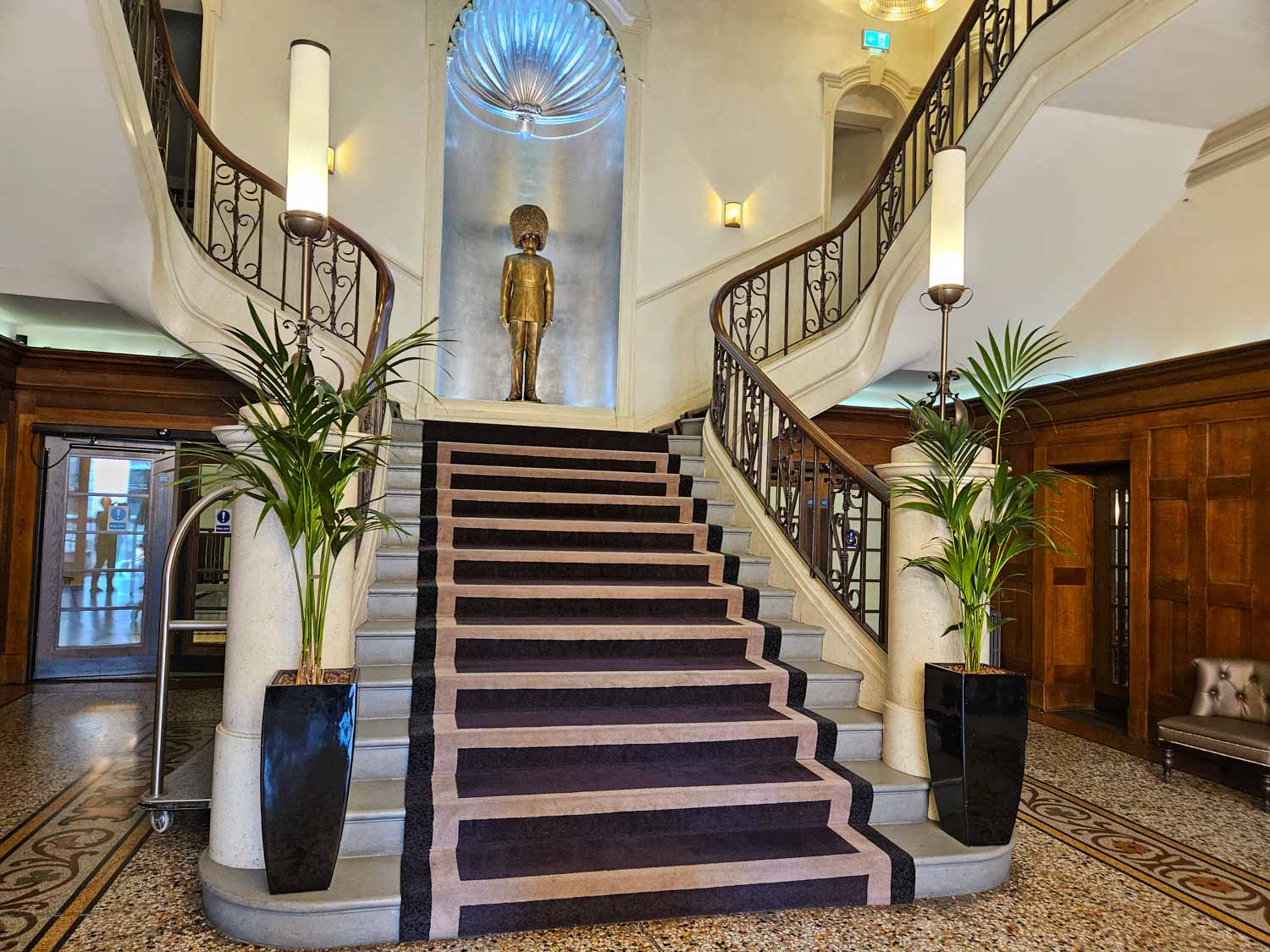 Grand staircase in the lobby with pot plants and golden coloured statue of a guard wearing a bearskin hat - my Courthouse Hotel Shoreditch review