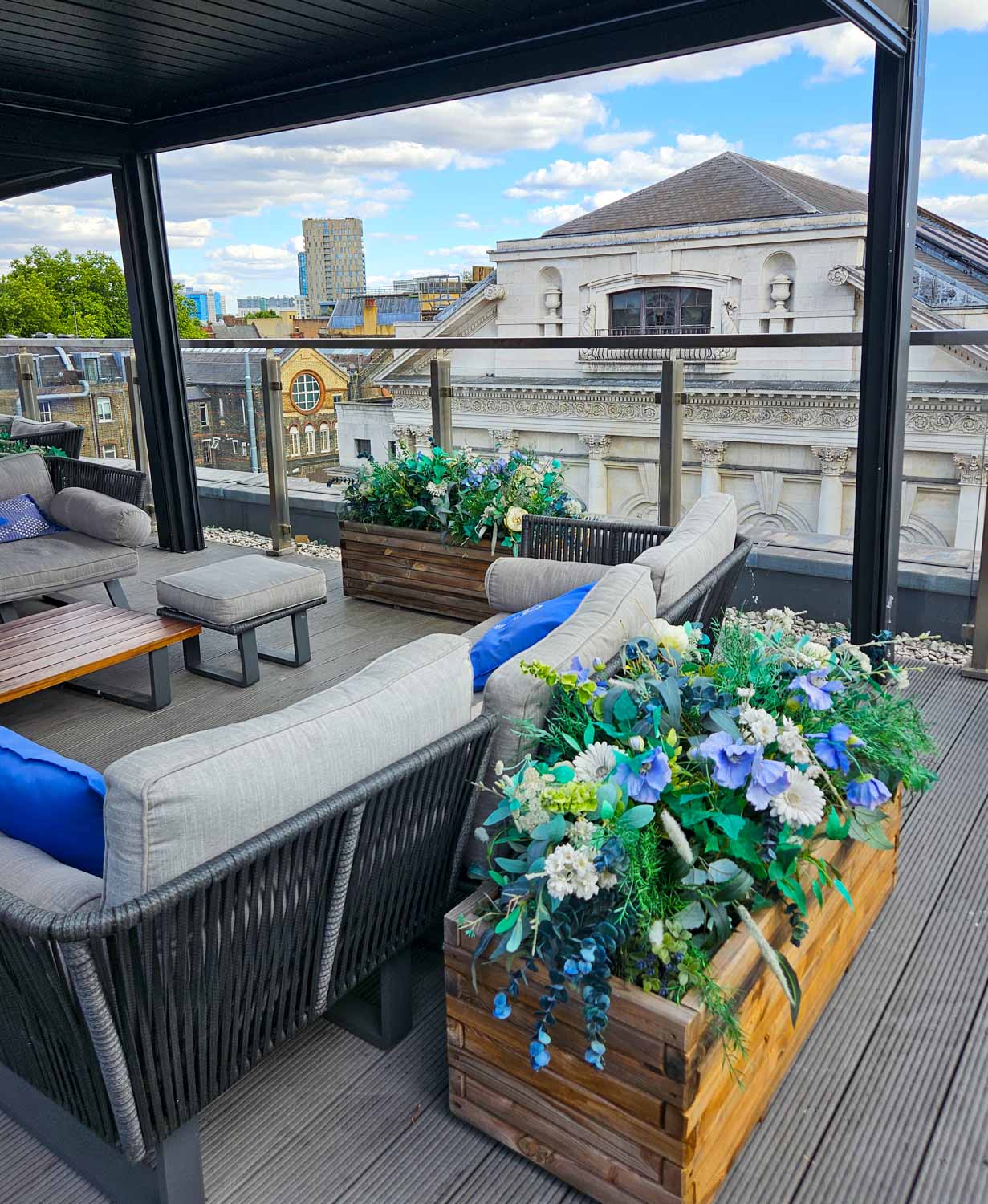 Planters of flowers and comfortable seats with the roof of Shoreditch Town Halla nd other buildings just seen from the hotel roof terrace - my Courthouse Hotel Shoreditch review