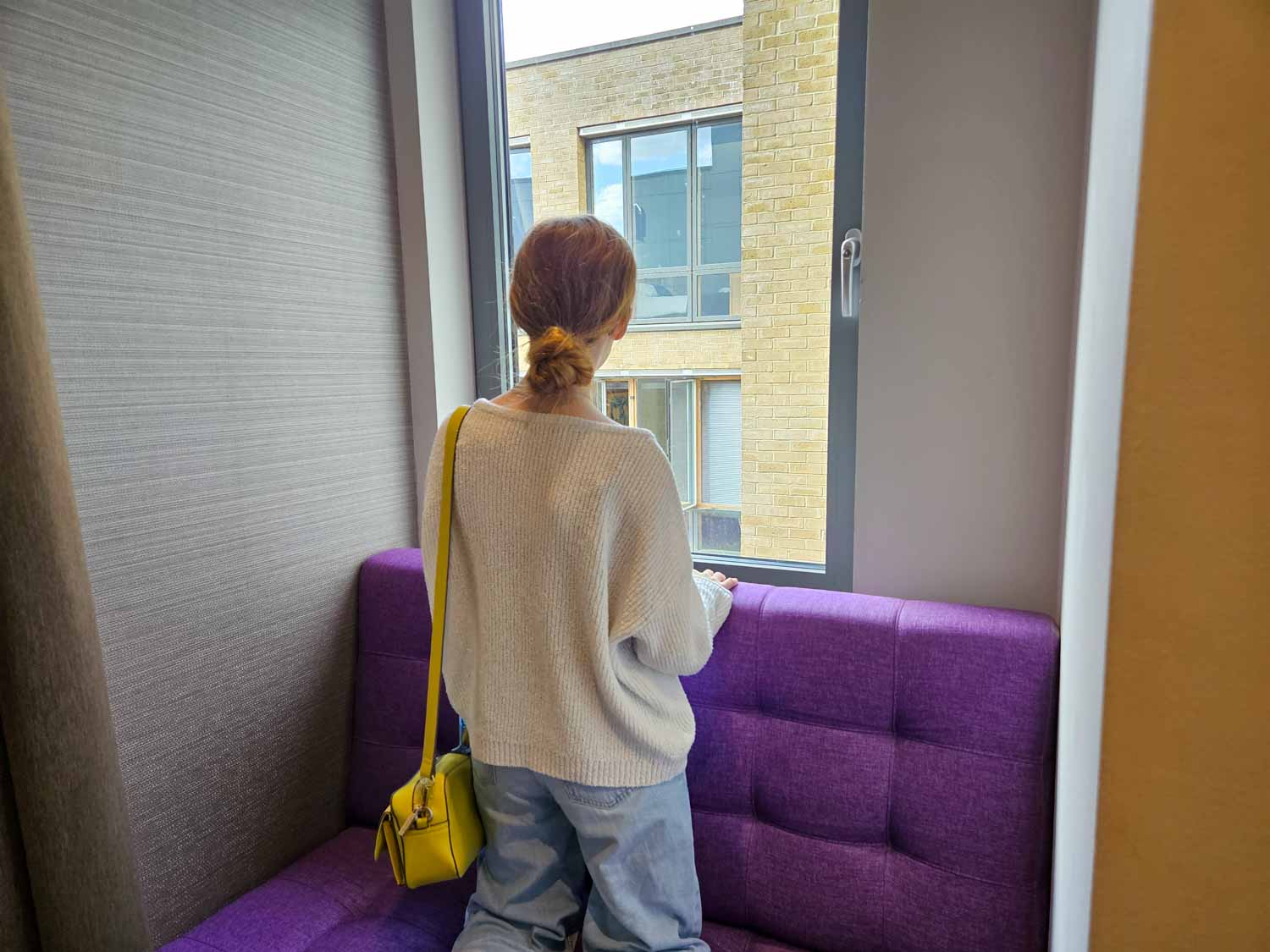 My daughter kneels on the purple window seat and looks out of the window of our suite - my Courthouse Hotel Shoreditch review and why it's great in London with teens