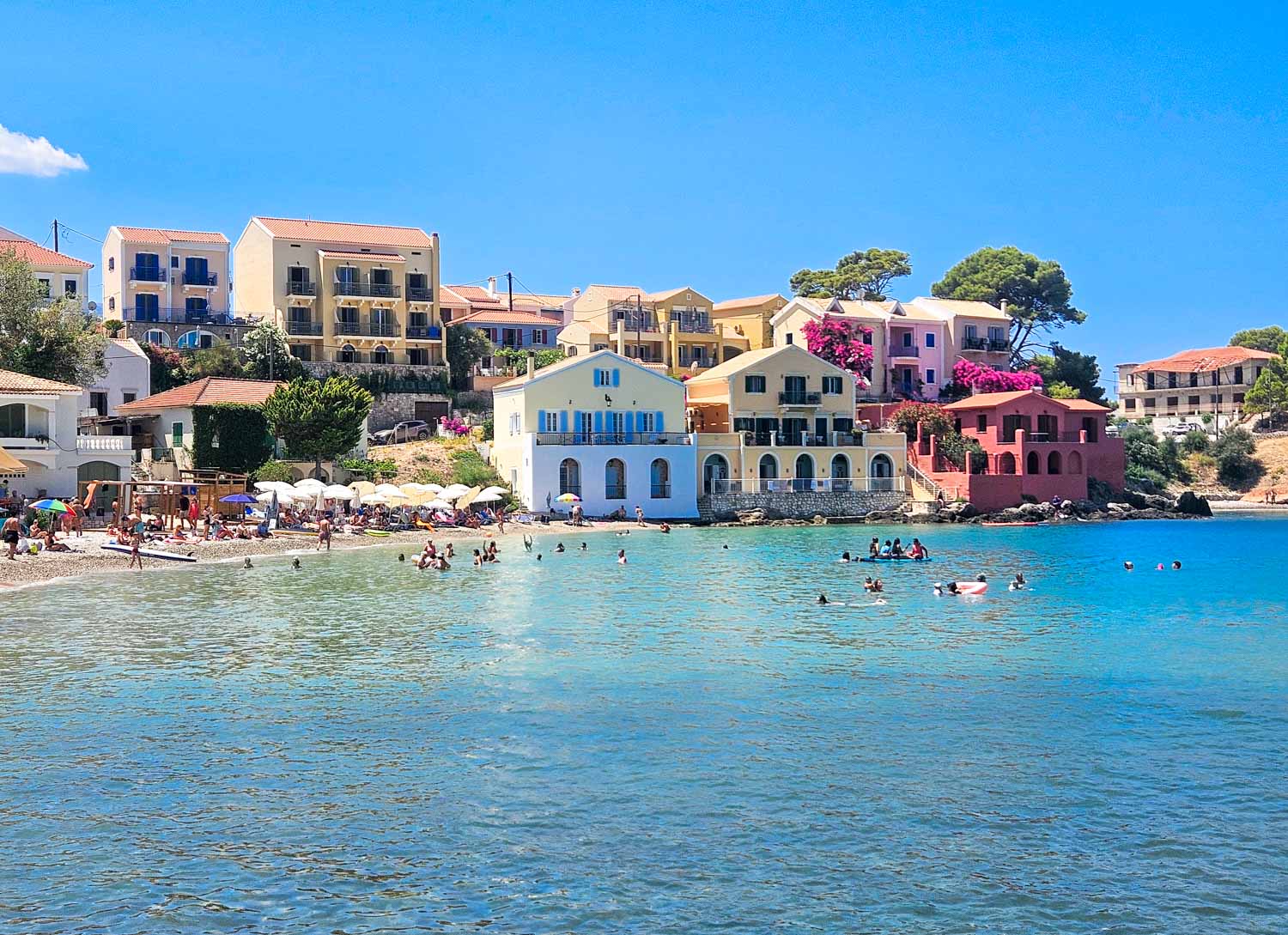 View across the sea to the small beach and colourful houses of Assos in Kefalonia - it's easy to combine a day out in Assos and Fiskardo with kids