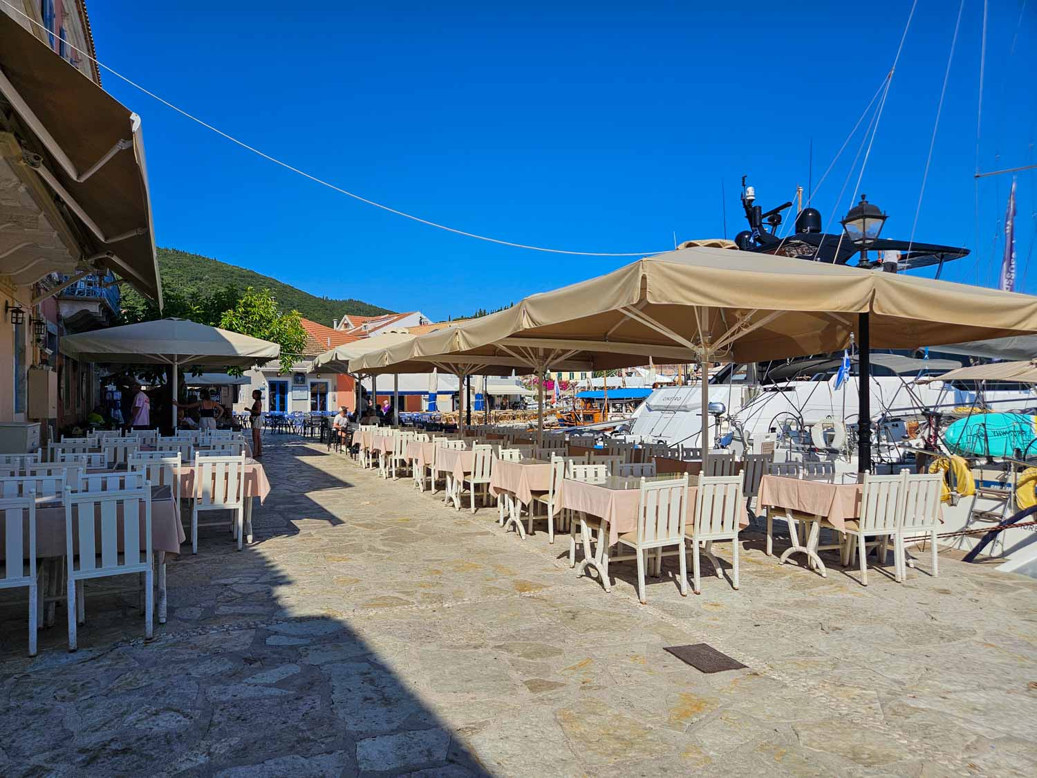 Tables under umbrellas at one of the many cafes and restaurants by the water in the harbour - what to do during one day in Fiskardo with kids