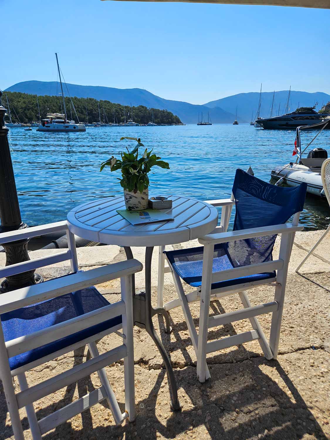 View across a table and chairs in a cafe right by the water's edge at the harbour - what to do during one day in Fiskardo with kids