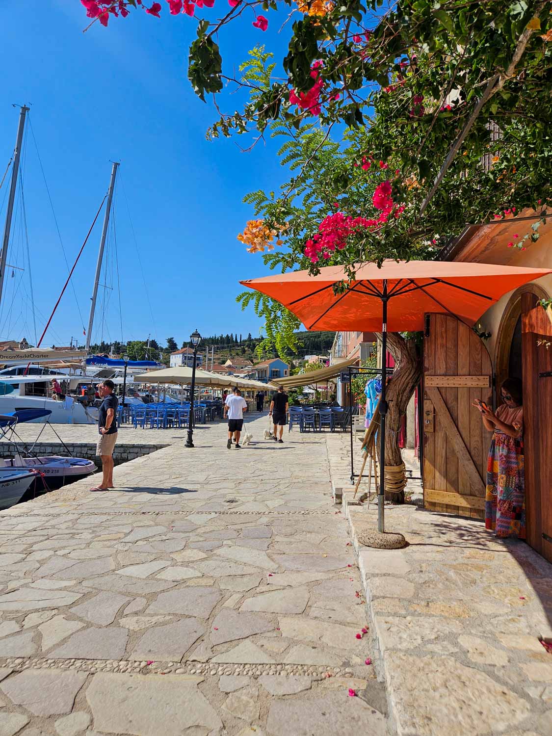View of shops and cafes under bright flowers along the harbour - what to do during one day in Fiskardo with kids