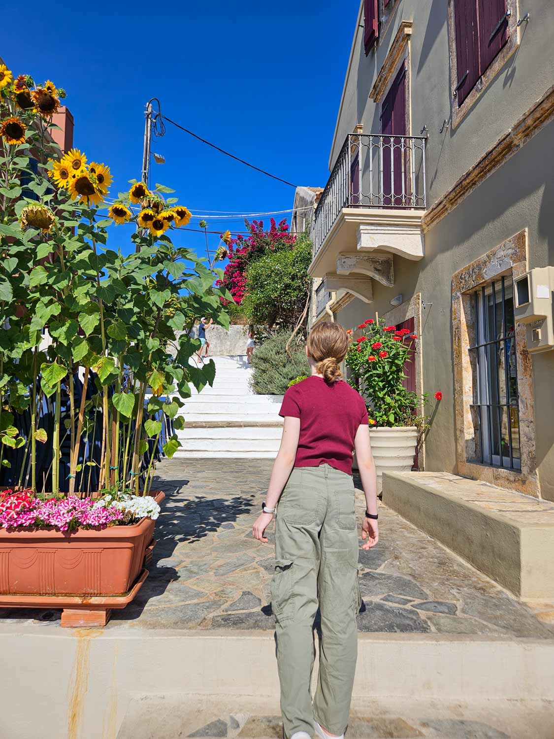 My daughter stands at the bottom of steps by some huge sunflowers - what to do during one day in Fiskardo with kids