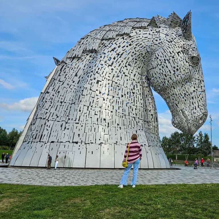 My daughter stands looking at the huge horse statues known as the Kelpies - my pick for the best things to do in Falkirk with kids
