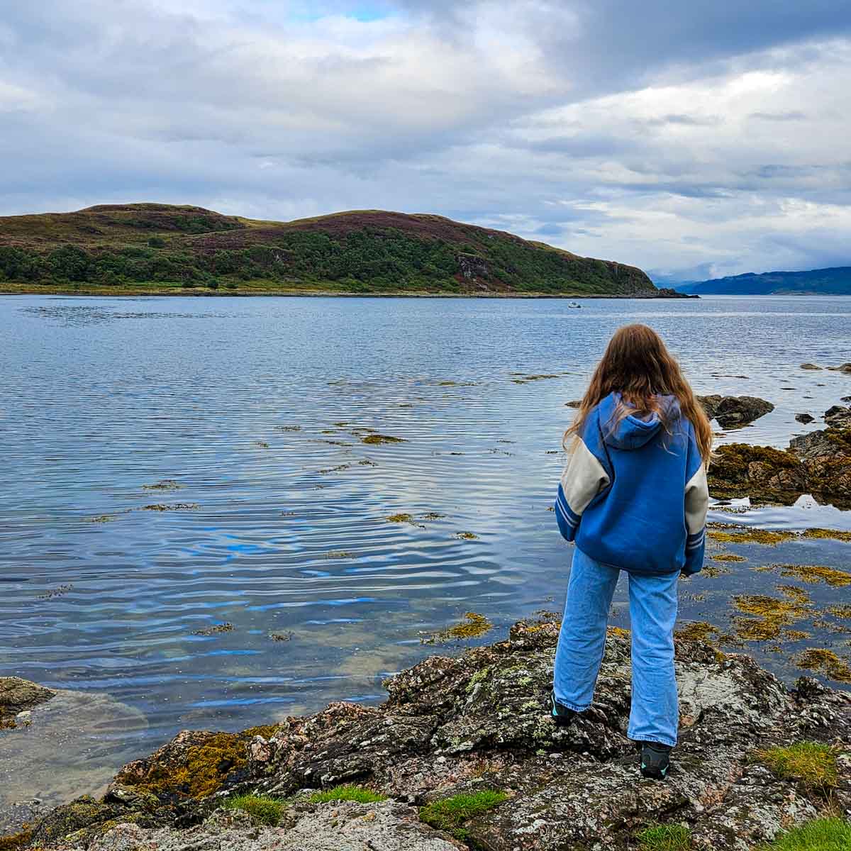 My daughter looks across the water near Isleornsay on the Isle of Skye to the hills beyond - my tips for the best things to do in the Isle of Skye with kids